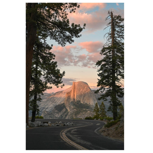 Winding road leading to a mountain peak with trees on a clear sky background